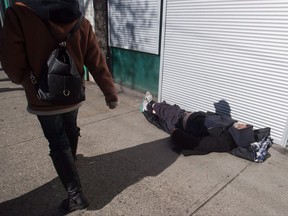 A woman walks past a man sleeping on the street in the Downtown Eastside of Vancouver, B.C., on Tuesday, February 21, 2017. Cities struggling to house their homeless are asking the federal Liberals to rethink the government's cornerstone homelessness program amid concerns about burdensome reporting requirements and inadequate funding models.THE CANADIAN PRESS/Darryl Dyck
