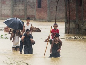Nepalese men carry children on their shoulders as they wade through flood waters in village Ramgadhwa in Birgunj, Nepal, Sunday, Aug. 13, 2017. An official said torrential rain, landslides and flooding have killed dozens of people in Nepal over the past three days, washing away hundreds of homes and damaging roads and bridges across the Himalayan country. (AP Photo/Manish Paudel)