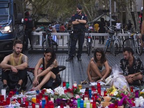 A police officer stands guard as people sit next to candles and flowers placed on the ground, after a terror attack that killed 14 people and wounded over 120 in Barcelona, Spain, Sunday, Aug. 20, 2017.