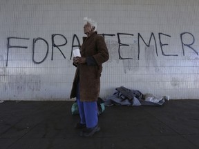 A homeless person stands in front of graffiti that reads in Portuguese "Temer Out," in Brasilia, Brazil, Tuesday, Aug. 1, 2017. Brazilian President Michel Temer faces a congressional vote on his future Wednesday, a showdown coming in a month dreaded by leaders of Latin America's largest nation, August has seen Brazilian presidents be impeached, resign and even kill themselves. (AP Photo/Eraldo Peres)