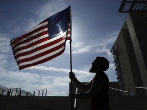FILE - In this April 10, 2017 file photo, a protester holds up a flag outside of a federal courthouse in Las Vegas in support of defendants accused of wielding weapons against federal agents during a 2014 standoff involving cattleman and states' rights advocate Cliven Bundy. A federal jury in Las Vegas is deliberating again Monday, Aug. 21, 2017, in the retrial of four men accused of wielding assault weapons against federal agents in a 2014 standoff near the Nevada ranch of anti-government figure Cliven Bundy. Jurors returned to work Monday, after spending a little more than two days last week going over five weeks of evidence in the case against four defendants. (AP Photo/John Locher, File)