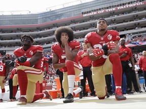 FILE - In this Oct. 2, 2016, file photo, from left, San Francisco 49ers outside linebacker Eli Harold, quarterback Colin Kaepernick, center, and safety Eric Reid kneel during the national anthem before an NFL football game against the Dallas Cowboys in Santa Clara, Calif. What started as a protest against police brutality has mushroomed a year later into a divisive debate over the future of Kaepernick who refused to stand for the national anthem and now faces what his fans see as blackballing for speaking out in a country roiled by racial strife. The once-rising star and Super Bowl quarterback has been unemployed since March, when he opted out of his contract and became a free agent who could sign with any team. (AP Photo/Marcio Jose Sanchez, File)