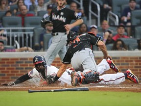 Atlanta Braves' Brandon Phillips (4) beats the tag from Miami Marlins catcher J.T. Realmuto (11) to score on a Nick Markakis ground ball during the first inning of a baseball game Friday, Aug. 4, 2017, in Atlanta. (AP Photo/John Bazemore)