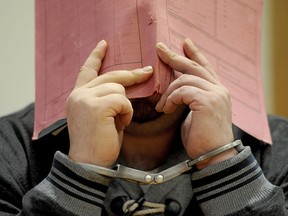 In this Dec. 9, 2014 file photo, former nurse Niels Hoegel accused of multiple murder and attempted murder of patients, stands in the court room wearing handcuffs and covering his face with a file at the district court in Oldenburg, Germany. Niels Hoegel., accused of multiple murder and attempted murder of patients, covering his face with a file at the district court in Oldenburg, Germany. Authorities now believe he was responsible for as many as 84 murders.
