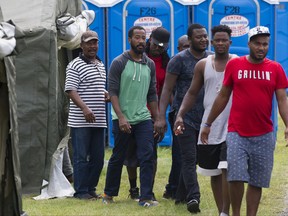 Asylum seekers step out of a tent to receive lunch at the Canada-United States border in Lacolle, Que. Thursday, August 10, 2017.