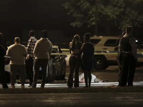 In this Sunday, Aug. 20, 2017, photo, a group of people and police officers stand near the body of a man fatally shot in the parking lot of an event center in Chicago. Several others were shot and transported to area hospitals in one of several shootings over the weekend in the city. (John J. Kim/Chicago Tribune via AP)