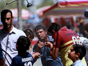 In this photo taken on Friday, July 28, 2017, people cool off by using an open air shower to beat the heat in Baghdad, Iraq. Iraq's weather service warned Thursday that temperatures will increase next week in most parts of the country, with the highs expected to reach 51 degrees Celsius.