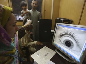 A Pakistani official with the United Nations High Commissioner for Refugees helps an Afghan refugee boy take a bio-metric scan at a repatriation center in Peshawar, Pakistan on Wednesday, Aug. 16, 2017. The UNHCR is working to help Afghan refugees who fled their country due to fighting and famine return home. (AP Photo/Muhammad Sajjad)