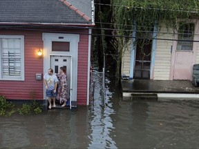FILE - In this Saturday, Aug. 5, 2017, file photo people stand outside their home in floodwaters in New Orleans. With more rain in the forecast and city water pumps malfunctioning after weekend floods, New Orleans' mayor is urging residents of some waterlogged neighborhoods to move their vehicles to higher ground. Mayor Mitch Landrieu's office said early Thursday, Aug. 10, 2017, the city has lost service to one of its power turbines, which powers most of the pumping stations service the East Bank of New Orleans. (Brett Duke/NOLA.com The Times-Picayune via AP, File)