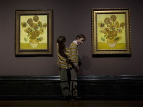 FILE - In this Friday, Jan. 24, 2014 file photo, twins Edgar, left, and Gabriel, aged 10, arrange themselves to pose for photographers beside two versions of Dutch-born painter Vincent van Gogh's "Sunflowers", the left one from 1888 and the right one from 1889, during a photocall at the National Portrait Gallery in London. Five versions of a Vincent van Gogh masterpiece are being reunited for the first time in a "virtual exhibition." On Monday, Aug. 14, 2017, they will all be streamed to a global audience in a Facebook Live broadcast. (AP Photo/Matt Dunham, File)