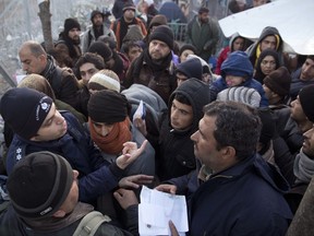 FILE - In this Wednesday, March 2, 2016 file photo, a Greek police officer checks registration papers as refugees crowd to cross the border from the Greek side to Macedonia at the northern Greek border station of Idomeni. EU countries have begun the process of sending migrants who arrived in Europe via Greece over the last five months back to have their asylum applications assessed there, it was announced on Tuesday, Aug. 8, 2017. Under EU rules, migrants must apply for asylum in the country they first enter. But the rules were suspended as hundreds of thousands of people, many Syrian refugees, entered Greece in 2015. (AP Photo/Petros Giannakouris, file)