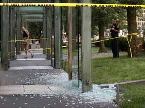 A passerby, left, and a law enforcement official, right, stand near broken glass at the New England Holocaust Memorial on Monday, Aug. 14, 2017, in Boston. Police say a person is in custody for allegedly vandalizing the memorial. It's the second time the memorial has been damaged this summer. Police say the suspect smashed a glass panel Monday. (AP Photo/Steven Senne)