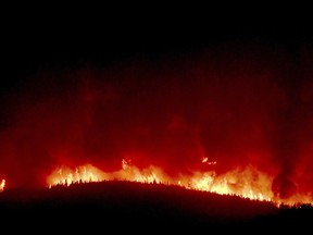 A wall of flames hundreds of feet high burn on a ridge above Rowan Road south of Lolo, Montana, early Thursday, Aug. 17, 2017. About 400 homes south and west of Lolo were evacuated because of the proximity of the Lolo Peak fire. (Kurt Wilson /The Missoulian via AP)