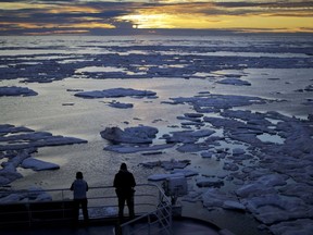 In this July 21, 2017 photo, researchers look out from the Finnish icebreaker MSV Nordica as the sun sets over sea ice floating on the Victoria Strait along the Northwest Passage in the Canadian Arctic Archipelago.