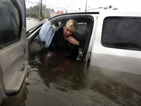 FILE - In this Monday, Aug. 28, 2017, file photo, Rhonda Worthington talks on her cellphone with a 911 dispatcher as she gets out of her car after her vehicle become stalled in rising floodwaters from Harvey in Houston. Cellphone networks are largely functional in the Texas and Louisiana regions hit by Harvey, as cellphone companies brought in supplemental equipment and backup power and turned to drones to diagnose problems. (AP Photo/LM Otero, File)
