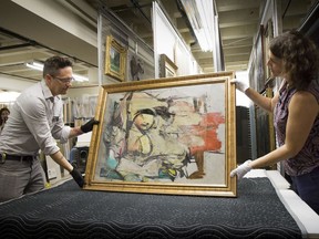 In this Aug. 9, 2017 photo provided by the University of Arizona, Willem de Kooning's "Woman-Ochre"  is readied for examination by Nathan Saxton, right, an exhibitions specialist, and Kristen Schmidt, a registrar, in Phoenix. More than three decades after thieves made off with the valuable painting from the University of Arizona Museum of Art, officials have recovered the long sought piece from an antique dealer in New Mexico.  (University of Arizona via AP)