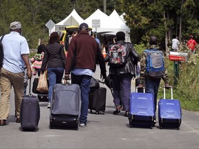 A family from Haiti approach a tent in Saint-Bernard-de-Lacolle, Quebec, stationed by Royal Canadian Mounted Police, as they haul their luggage down Roxham Road.