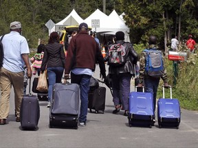 A family from Haiti approach a tent in Saint-Bernard-de-Lacolle, Quebec, stationed by Royal Canadian Mounted Police, as they haul their luggage down Roxham Road in Champlain, N.Y., Monday, Aug. 7, 2017.