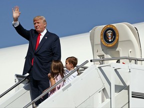 FILE- In this Aug. 4, 2017, file photo, President Donald Trump waves as he walks down the steps of Air Force One with his grandchildren, Arabella Kushner, center, and Joseph Kushner, right, after arriving at Morristown Municipal Airport to begin his summer vacation at his Bedminster golf club in Morristown, N.J. The president has decamped from Washington to his private golf club in central New Jersey. But he has repeatedly pushed back on the idea that this is a relaxing August getaway. (AP Photo/Evan Vucci, File)