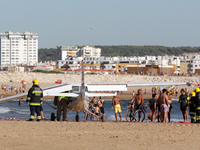 Firefighters stand next to a small plane after an emergency landing on Sao Joao beach that killed a 56-year-old man and an 8-year-old girl who were sunbathing in Costa da Caparica, outside Lisbon, Wednesday, Aug. 2, 2017.