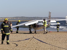 Firefighters stand next to a small plane after an emergency landing on Sao Joao beach in Costa da Caparica, outside Lisbon, Wednesday, Aug. 2, 2017.