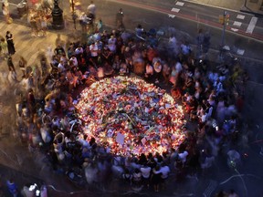 People gather at a memorial tribute of flowers, messages and candles to the victims on Barcelona's historic Las Ramblas promenade on the Joan Miro mosaic, embedded in the pavement where the van stopped after killing at least 13 people in Barcelona , Spain, Friday, Aug. 18, 2017. Spanish police on Friday shot and killed five people carrying bomb belts who were connected to the Barcelona van attack as the manhunt intensified for the perpetrators of Europe's latest rampage claimed by the Islamic State group. (AP Photo/Manu Fernandez)