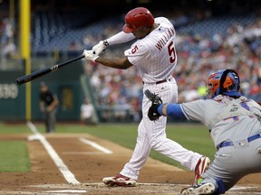 Philadelphia Phillies' Nick Williams, left, follows through after hitting an RBI-single off New York Mets starting pitcher Seth Lugo during the first inning of a baseball game, Friday, Aug. 11, 2017, in Philadelphia. Mets catcher Rene Rivera, right, looks on. (AP Photo/Matt Slocum)