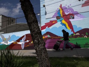 In this Aug. 13, 2017 photo, a man walks past a mural that is being painted by asylum seekers along with Mexican artist Eva Bracamontes in Mexico City. The migrant mural project, which has already completed works in other Mexican towns, is meant to help give a voice to migrants in Mexico, most of them central Americans fleeing violence, and create more understanding of their motivations and experiences. (AP Photo/Rebecca Blackwell)