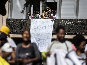 Migrants hang a banner with writing reading in Italian "we are not terrorists, we want housing" from a balcony of a building in downtown Rome, Wednesday, Aug. 23, 2017. Rome officials are defending their decision to evacuate hundreds of refugees occupying an abandoned building in the city center after protests from the U.N. refugee agency, UNICEF and humanitarian organizations. (Angelo Carconi/ANSA via AP)
