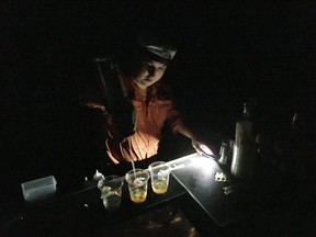 Downtown Houston bar owner William Bedner pours a round of whiskeys by flashlight in this photo taken on Aug. 28, 2017. Bedner's bar lost power as Tropical Storm Harvey flooded the streets just blocks from his bar Lilly & Bloom. Bedner has kept pouring drinks for friends, but expects to lose a lot of business and money due to the devastation wrought by the storm. (AP Photo/Jason Dearen)