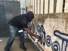 In this Wednesday, Aug. 2, 2017, photo Tyree Colion spray paints the words "No Shoot Zone" on a brick wall behind a convenience store, in a spot near where a 13-year-old girl was fatally shot in Baltimore County, Md. County police later arrested Colion for what they say was destruction of property, although he claimed he was given permission to paint the wall by a store clerk. (AP Photo/Juliet Linderman)