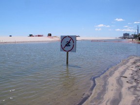 This July 31, 2017 photo shows a no swimming sign in one of numerous large pools of water that have formed on the beach in Margate N.J. due to heavy rains. The water is blocked from draining into the ocean by new sand dunes being built as part of a storm protection program that Margate residents vigorously fought, claiming that the dunes would cause exactly the type of standing water that has occurred. (AP Photo/Wayne Parry)