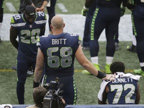 Seattle Seahawks center Justin Britt (68), and cornerback Jeremy Lane (20) stand near defensive end Michael Bennett (72) as Bennett sits on the bench during the national anthem before the team's NFL football preseason game against the Minnesota Vikings, Friday, Aug. 18, 2017, in Seattle. (AP Photo/Scott Eklund)