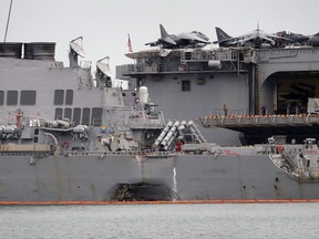 The damaged port aft hull of USS John S. McCain, left, is seen while docked next to USS America at Singapore's Changi naval base on Tuesday, Aug. 22, 2017 in Singapore. The focus of the search for 10 U.S. sailors missing after a collision between the USS John S. McCain and an oil tanker in Southeast Asian waters shifted Tuesday to the damaged destroyer's flooded compartments. (AP Photo/Wong Maye-E)