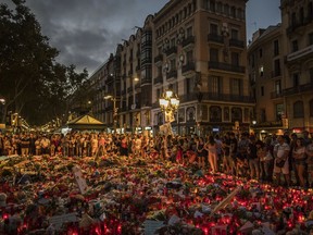 People stand next to candles and flowers placed on the ground, after a terror attack that left many killed and wounded in Barcelona, Spain, Monday, Aug. 21, 2017. The lone fugitive from the Spanish cell that killed 15 people in and near Barcelona was shot to death Monday after he flashed what turned out to be a fake suicide belt at two troopers who confronted him in a vineyard just outside the city he terrorized, authorities said. (AP Photo/Santi Palacios)