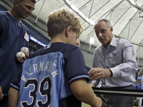 Baseball Commissioner Rob Manfred, right, signs autographs for fans while on his way to a news conference before a baseball game between the Tampa Bay Rays and the Toronto Blue Jays on Wednesday, Aug. 23, 2017, in St. Petersburg, Fla. (AP Photo/Chris O'Meara)