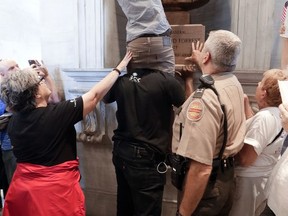 Justin Jones sits on the shoulders of a fellow protester as Jones tosses a sweatshirt over the bust of Nathan Bedford Forrest in the Capitol Monday, Aug. 14, 2017, in Nashville, Tenn.