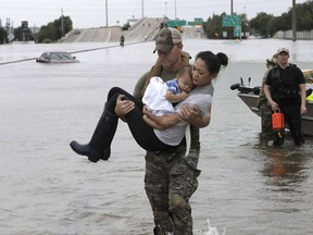 CORRECTS FROM CONNIE TO CATHERINE - Houston Police SWAT officer Daryl Hudeck carries Catherine Pham and her 13-month-old son Aiden after rescuing them from their home surrounded by floodwaters from Tropical Storm Harvey Sunday, Aug. 27, 2017, in Houston. The remnants of Hurricane Harvey sent devastating floods pouring into Houston Sunday as rising water chased thousands of people to rooftops or higher ground. (AP Photo/David J. Phillip)