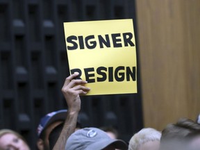 A sign asks Mayor Mike Signor to resign during the Charlottesville City Council meeting Monday, Aug. 21, 2017, in Charlottesville, Va. Anger boiled over at the first Charlottesville City Council meeting since a white nationalist rally in the city descended into violent chaos, with some residents screaming and cursing at councilors Monday night and calling for their resignations. (Andrew Shurtleff/The Daily Progress via AP)