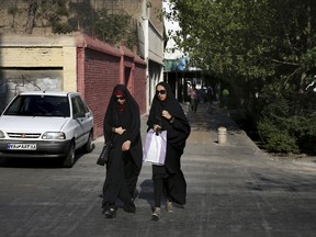 In this Thursday, Aug. 24, 2017, photo, two Iranian women cross a street while wearing the "chador," a head-to-toe garment, in downtown Tehran, Iran. She is just a couple of weeks into her appointment as new Iranian vice president but Laaya Joneidi's decision to abandon her headscarf and fashion style for the all-encompassing black chador is raising questions among women in the Islamic Republic _ especially after she said that President Hassan Rouhani personally asked her to wear the more conservative Muslim women's garment.  (AP Photo/Vahid Salemi)