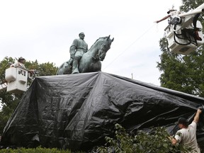 City workers drape a tarp over the statue of Confederate General Robert E. Lee in Emancipation park in Charlottesville, Va., Wednesday, Aug. 23, 2017.  The move to cover the statues is intended to symbolize the city's mourning for Heather Heyer, killed while protesting a white nationalist rally earlier this month.  (AP Photo/Steve Helber)