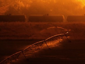 Irrigation sprinklers water a field as a wildfire burns on a hillside above stopped railcars near Othello, Wash., early Sunday, Aug. 13, 2017. (AP Photo/Ted S. Warren)