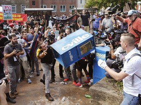 FILE - In this Aug. 12, 2017 file photo, white nationalist demonstrators clash with a counter demonstrator as he throws a newspaper box at the entrance to Lee Park in Charlottesville, Va. Weeks before a statue of Robert E. Lee in Charlottesville, Virginia, became a flashpoint in the nation's struggle over race and history, it already was a focus of emotional debate in the state's Republican primary election.  (AP Photo/Steve Helber, File)
