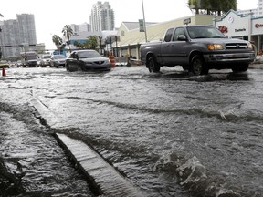FILE - In this Sept. 23, 2014, file photo, vehicles negotiate heavily flooded streets as rain falls in Miami Beach, Fla. Certain neighborhoods regularly experience flooding during heavy rains and extreme high tides. Directly contradicting President Donald Trump, a draft report produced by 13 federal agencies concludes that the United States is already feeling the negative impacts of climate change, with a stark increase in the frequency of heat waves and other extreme weather events over the last four decades. The assessment said global temperatures will continue to rise without steep reductions in burning fossil fuels, with increasingly negative impacts. (AP Photo/Lynne Sladky, File)