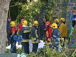 Firefighters hold a blanket as bodies are removed from the scene where a tree fell on a large crowd on the outskirts of Funchal, the capital of Madeira island, Portugal, Tuesday, Aug. 15, 2017. Portuguese authorities say a tree that fell during a popular religious festival on the island of Madeira killed at least 12 people and more than 50 others were injured in the accident near the island capital of Funchal. The tree fell while a large crowd was gathered as part of a Nossa Senhora do Monte festival.