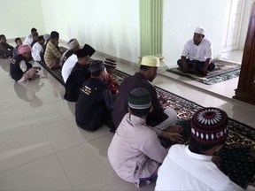 In this July 22, 2017, photo, former radical preacher Khairul Ghazali, top, delivers a sermon after an afternoon prayer at Al Hidayah Islamic Boarding School in Sei Mencirim, North Sumatra, Indonesia. Ghazali set up the school for the sons of Islamic militants whose fathers are either killed in raids or in prison for terrorism offenses aimed at preventing them from becoming the next generation of Indonesian jihadists. (AP Photo/Binsar Bakkara)
