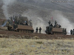 In this photo released Wednesday, Aug. 23, 2017, by the Lebanese Army official website, Lebanese soldiers sit a top armored personnel carriers during a battle against Islamic State militants, on the outskirts of Ras Baalbek, northeast Lebanon. Lebanon's prime minister has visited troops near his country's border with Syria, and said that victory against the Islamic State group is near. Arabic reads, "Army command, the Directorate of Orientation." (Lebanese Army Website via AP)