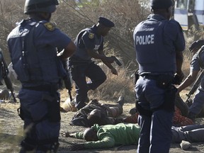 FILE - In this Aug. 16, 2012 file photo police surround the bodies of striking miners after opening fire on a crowd at the Lonmin Platinum Mine in Marikana, near Rustenburg, South Africa killing 34. Five years after the event rights groups say no one has been prosecuted and miners' living conditions are as "squalid" as ever. (AP Photo/File)