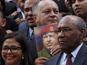 Venezuela's Constitutional Assembly delegate Diosdado Cabello, top center, holds a picture of late  President Hugo Chavez as he poses for the official group photo, on the front steps of the National Assembly in Caracas, Venezuela, Friday, Aug. 4, 2017. Venezuela's President Nicolas Maduro is heading toward a showdown with his political foes, after seating a loyalist assembly that will rewrite the country's constitution and hold powers that override all other government branches. Also pictured are Constitutional Assembly President Delcy Rodriguez and first Vice President Aristobulo Isturiz. (AP Photo/Ariana Cubillos)