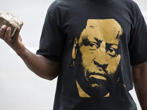 FILE- In this May 23, 2016 file photo, An opposition protester wearing a T-shirt of opposition leader Raila Odinga holds a rock, as he and others tried to gather outside the offices of the electoral commission before being tear-gassed away by police, in downtown Nairobi, Kenya. Odinga, the opposition leader who wants to be Kenya's next president, says he'll fight corruption and ethnic divisions. Yet he is also an enigmatic figure who was allegedly involved in an Aug. 1, 1982 coup attempt that exacerbated tensions in a country whose democracy remains vulnerable to ethnic feuding. (AP Photo/Ben Curtis, file)